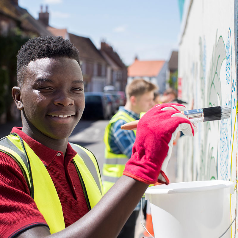 Smiling volunteer painting a community mural, representing Complex Community Federal Credit Union’s commitment to local service and member support.