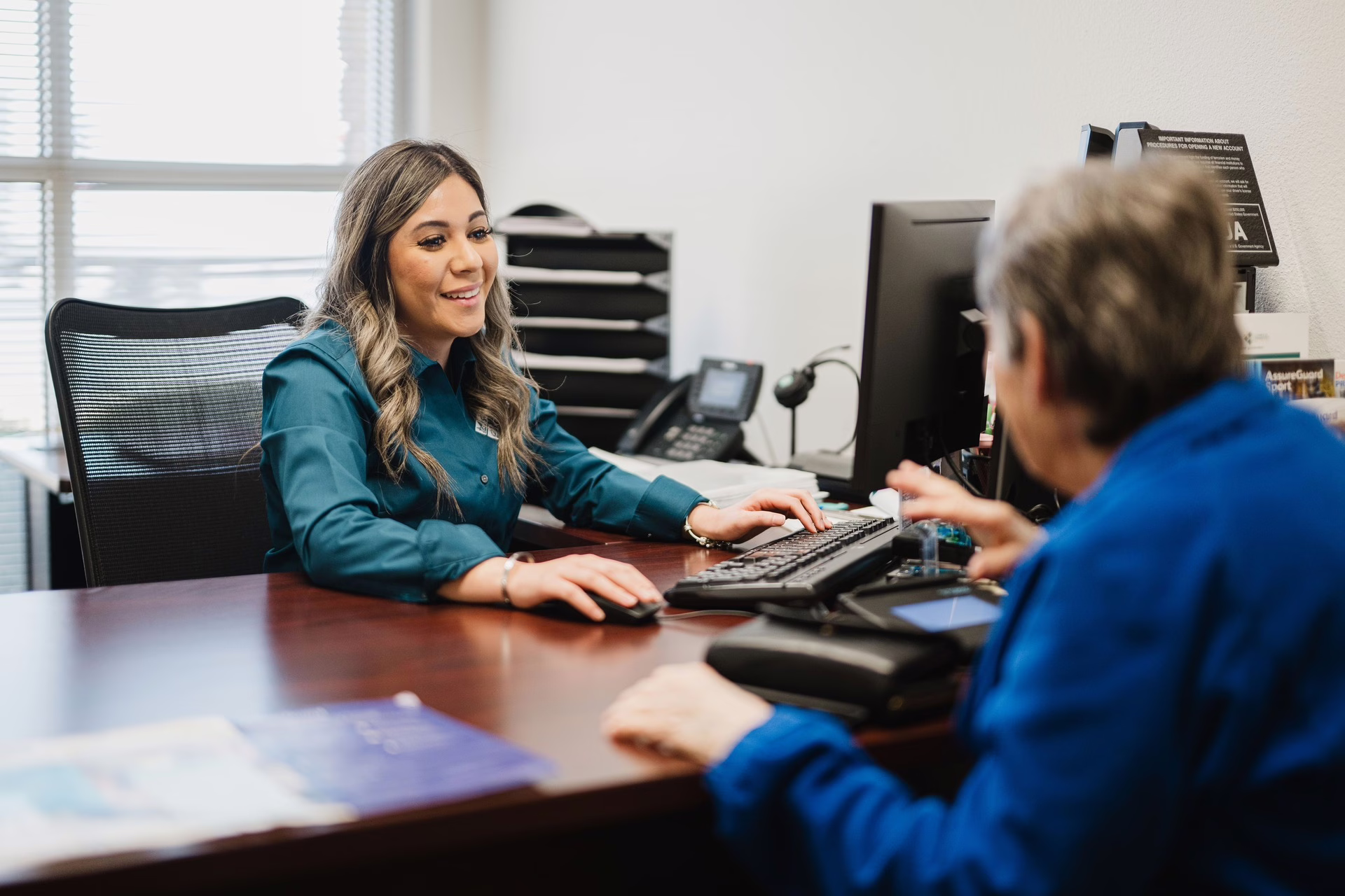 Woman holding phone in one hand while working on laptop